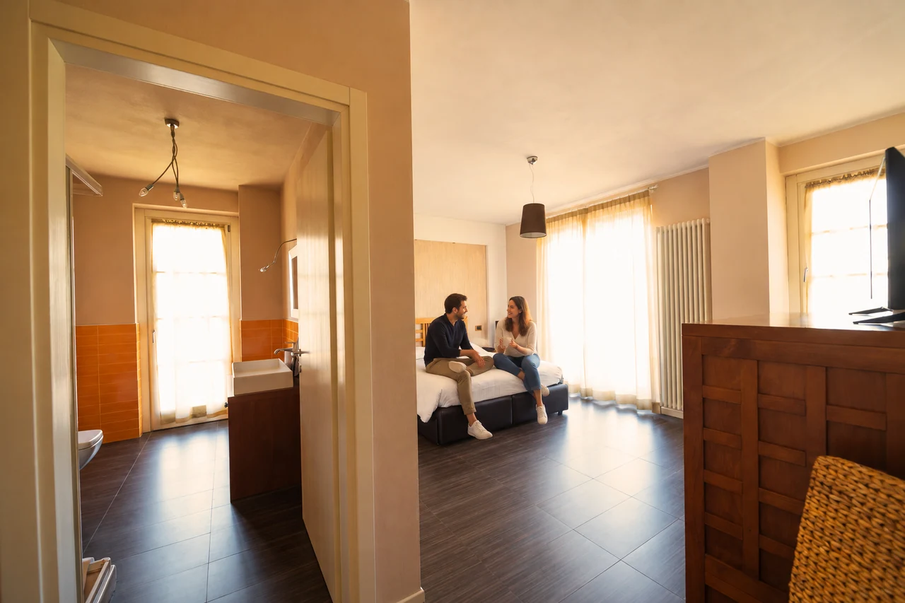 Camera T’Ami con coppia seduta sul letto; persone aggiunte con AI